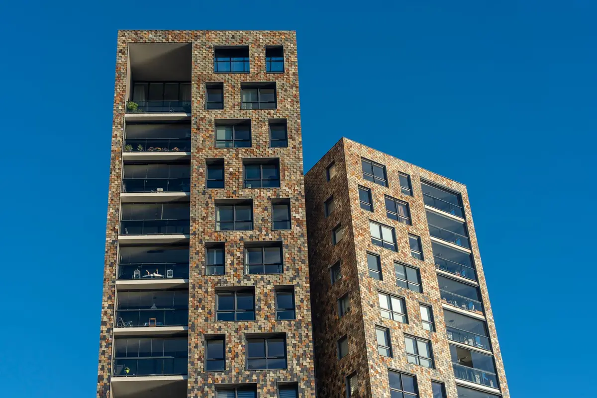 Two residential apartment towers with balconies viewed from below against a blue sky.