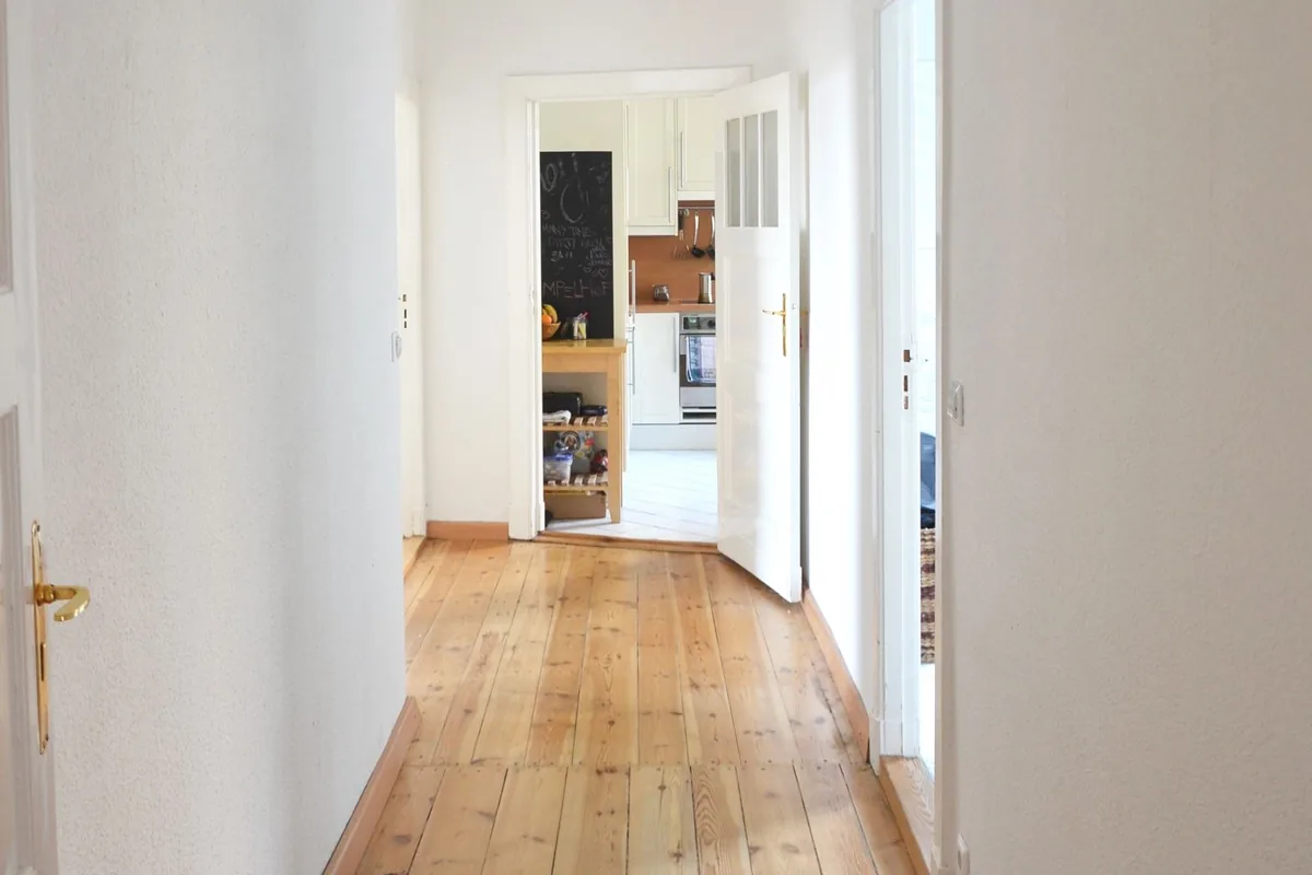 An empty apartment corridor with bare wooden floorboards running clear from end to end towards open doors.