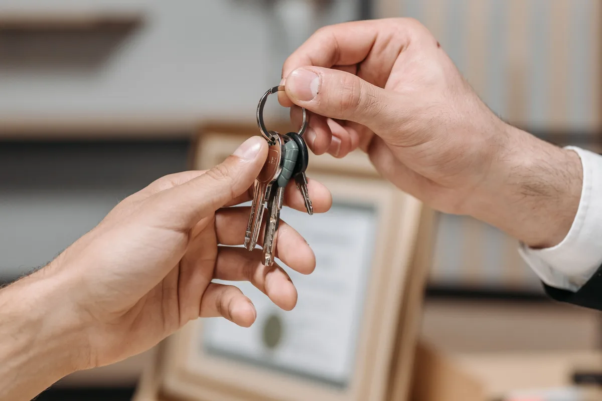 One person handing a set of house keys to another person standing in a doorway.