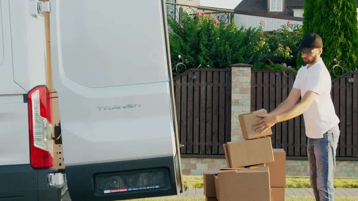 A man loading cardboard boxes into the back of a van outside a residential house.