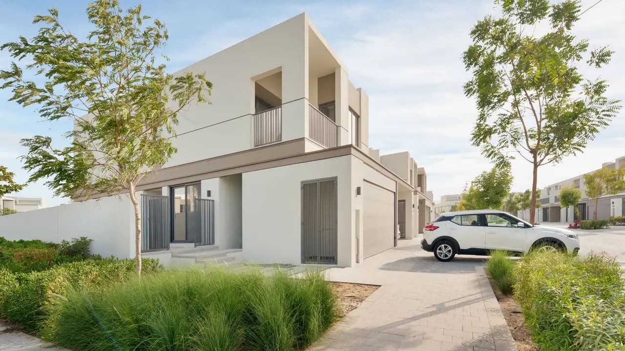 A modern two-storey villa with a driveway and parked car in a Dubai residential community.