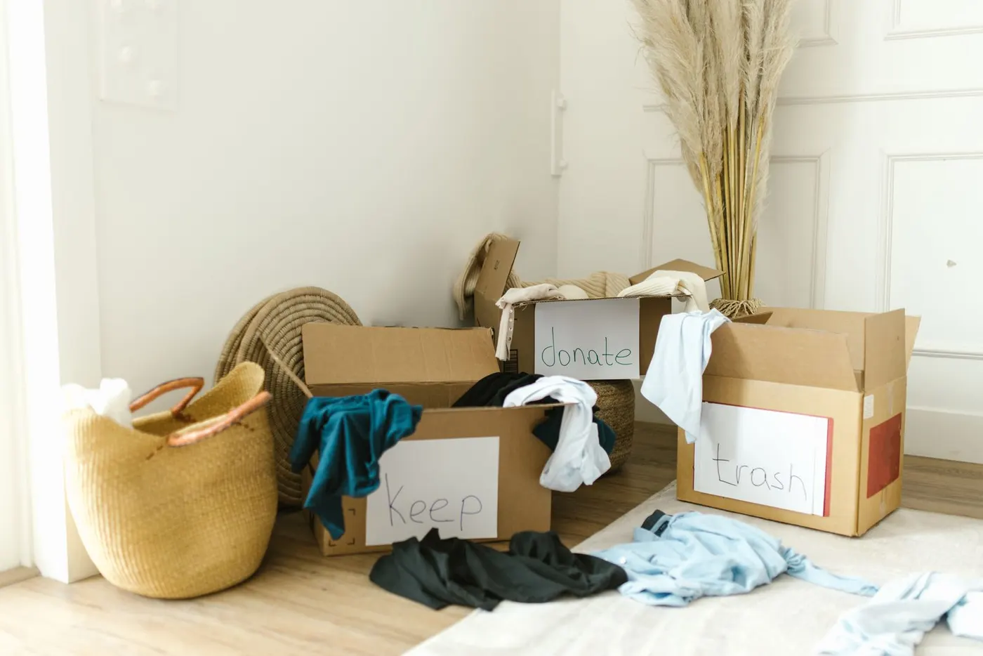Cardboard boxes labelled keep, donate and trash filled with clothes and household items.