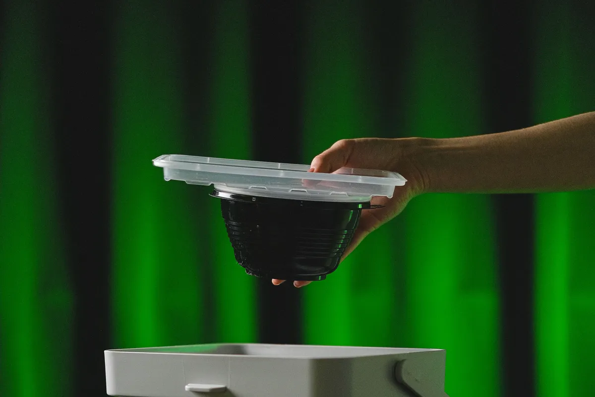 A hand placing a recyclable plastic container into a bin labelled for sorted waste.