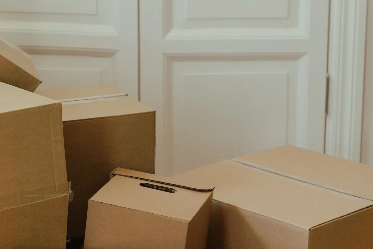 Cardboard boxes of several different sizes stacked on the floor in front of a closed white panelled door.