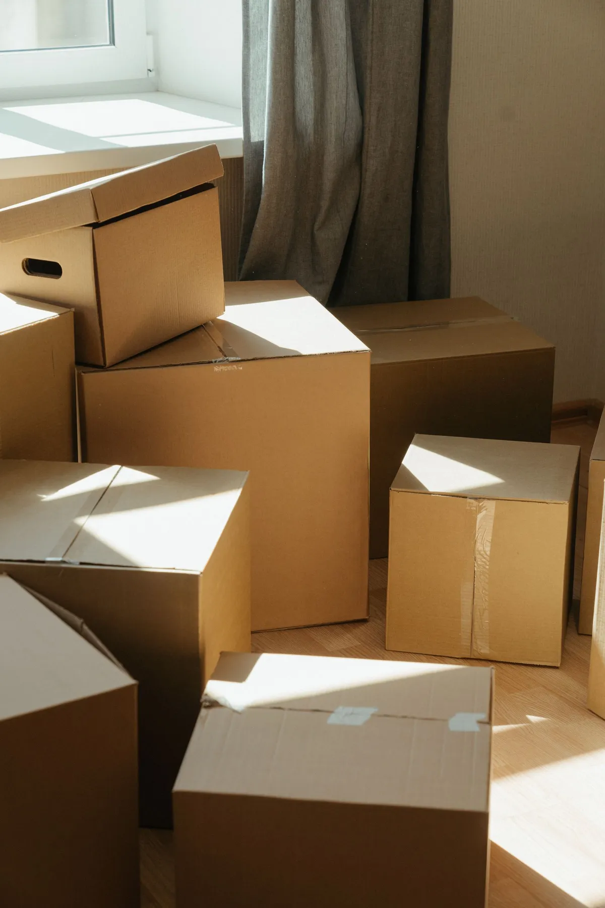 Several cardboard boxes of different sizes stacked together in a sunlit room, ready for collection.
