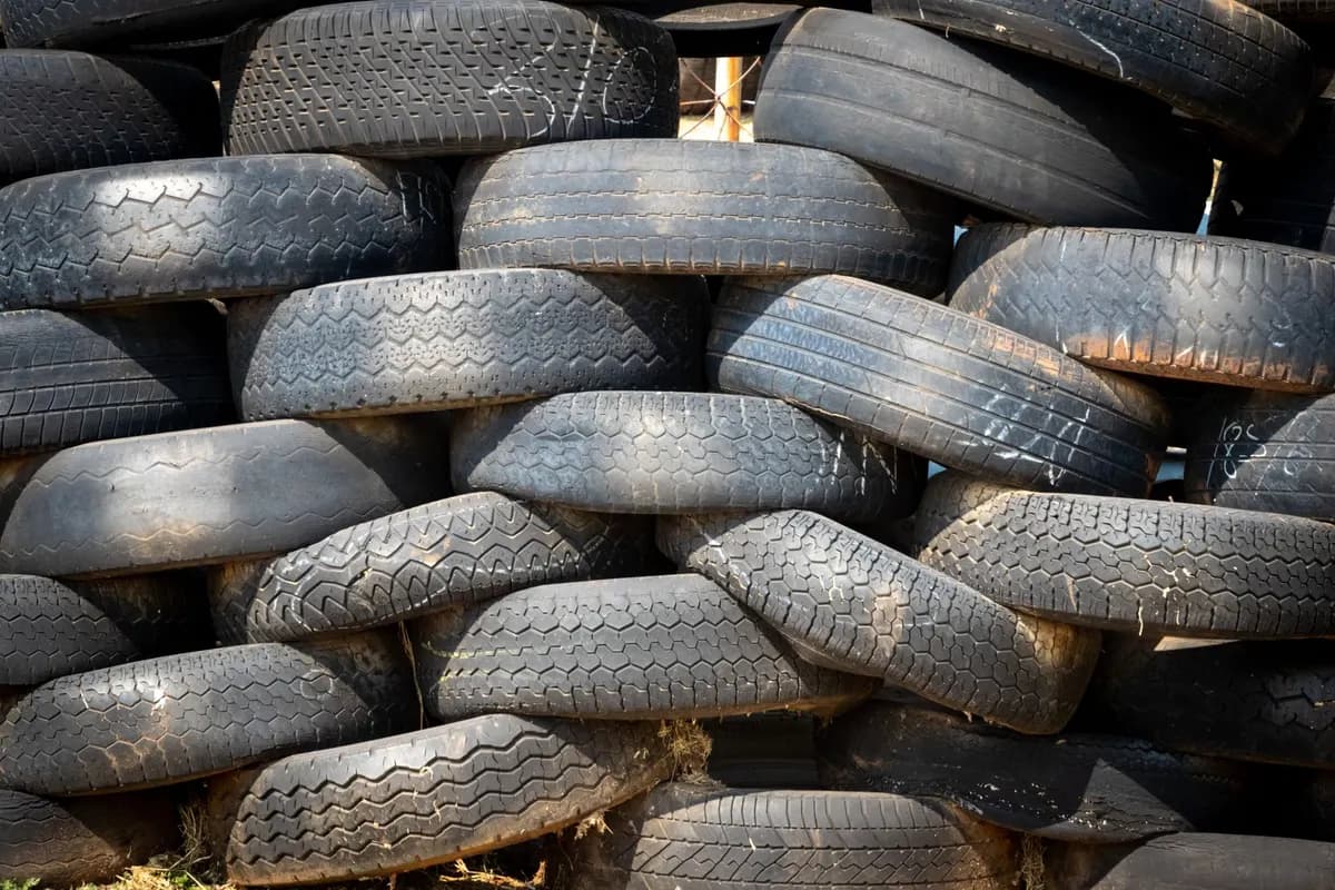 A wall of used car tyres stacked in overlapping rows outdoors in strong daylight.