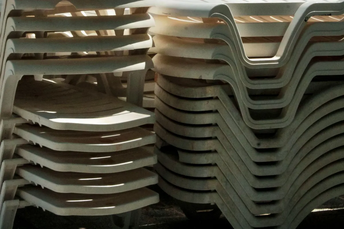 Stacks of sun-bleached white plastic sun loungers, discoloured and stained, photographed close up in bright light.