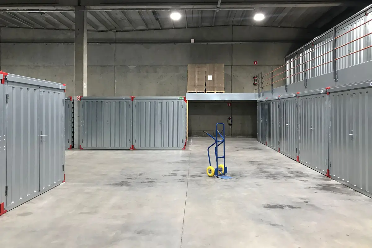 A wide concrete corridor running between two rows of grey metal storage units, with a single blue hand truck standing in the middle.