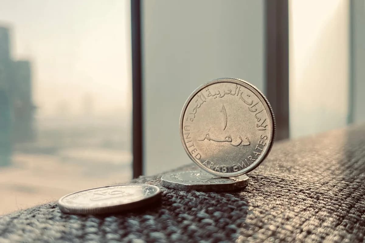 UAE dirham coins standing on a windowsill with the Dubai skyline blurred in the background.