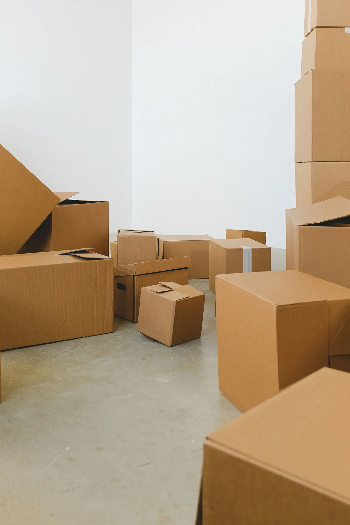 Dozens of cardboard boxes of different sizes stacked and scattered across the bare floor of an empty room.